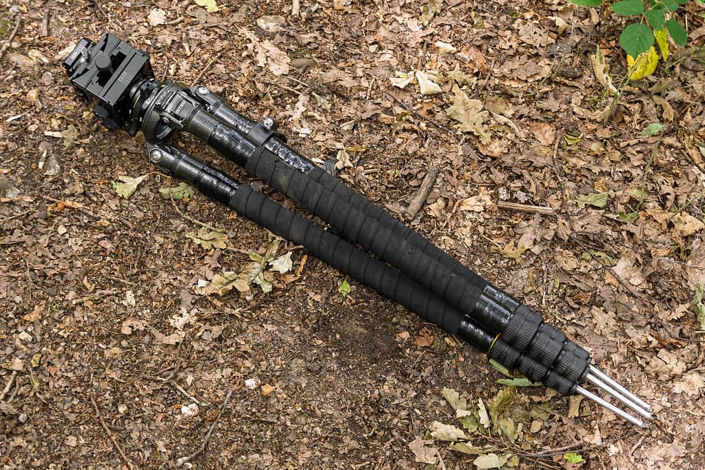 A olded Gitzo GT3531XLS tripod with foam grips and an Arca Swiss C1 Cube head - one of the best tripods for woodland photography. Its legs have spiked feet and are retracted amidst brown leaves and twigs.