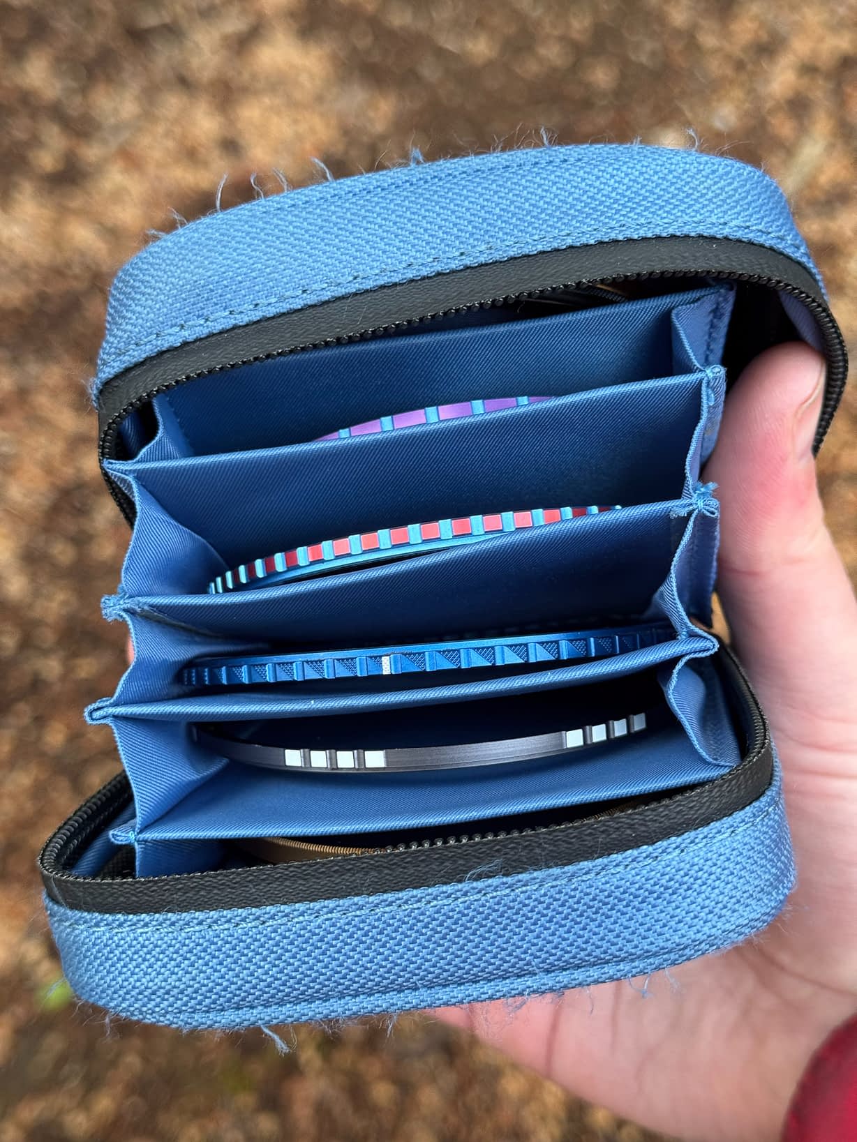 A blue zipped filter case with six sections, containing a mix of woodland photography filters. All of the filters are colour-coded according to their function and magnetic for easy switching or stacking. Blurred brown soil adds earthy tones from the forest floor.